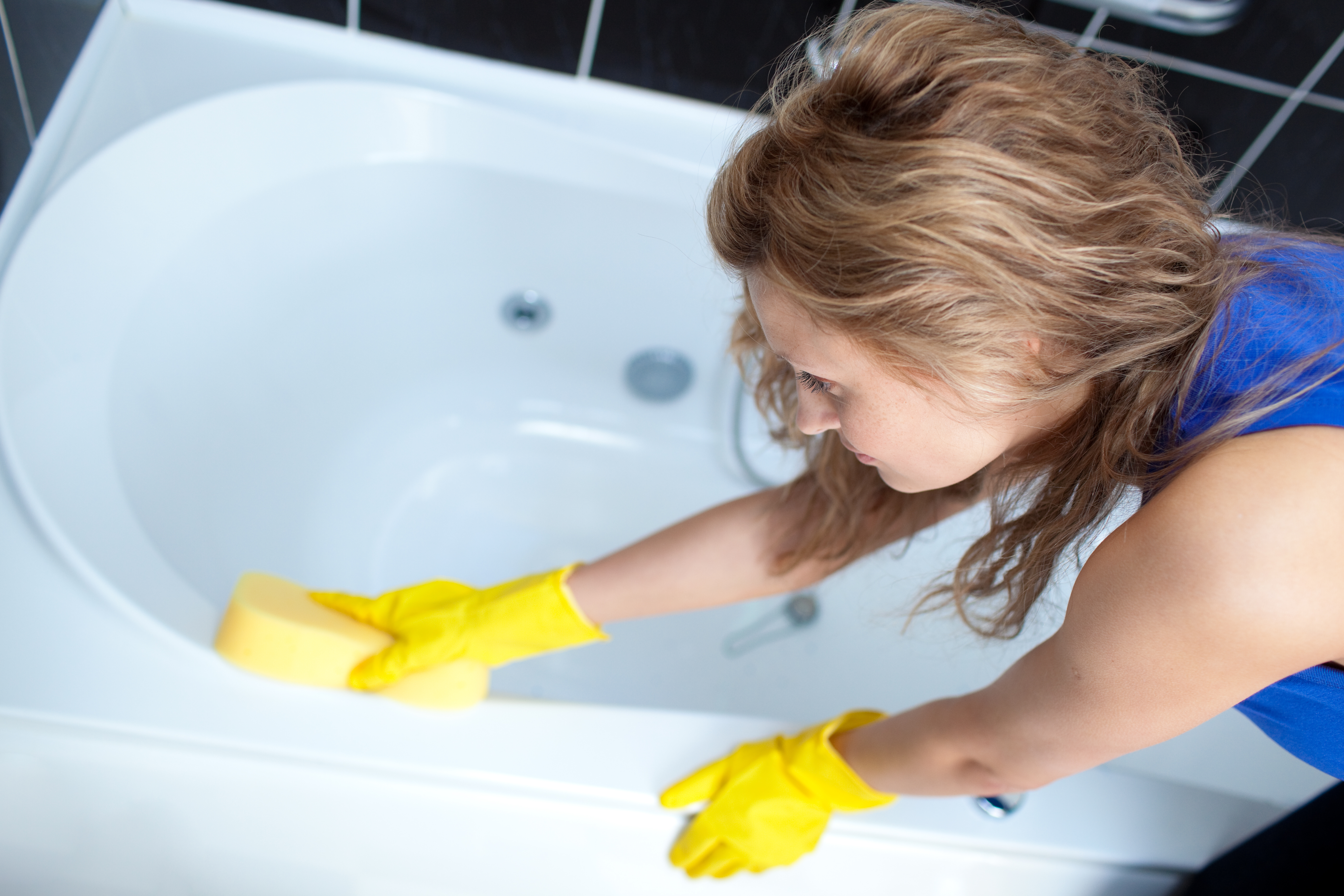 Woman cleaning bathtub with yellow gloves