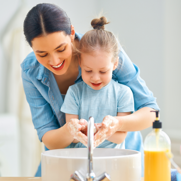 امرأة تعلّم فتاة صغيرة كيفية غسل يديها.